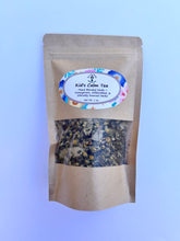 Load image into Gallery viewer, A pouch of Children's Calming Loose Leaf Tea surrounded by chamomile, lemon balm, and linden, styled on a natural wood background for a peaceful, earthy feel.

